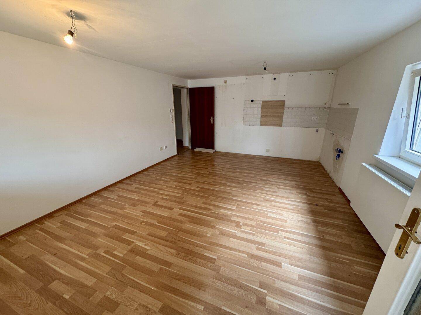 Offener Wohnbereich mit Laminatboden und vorbereiteter Küchenzeile, bietet viel Gestaltungspotenzial.