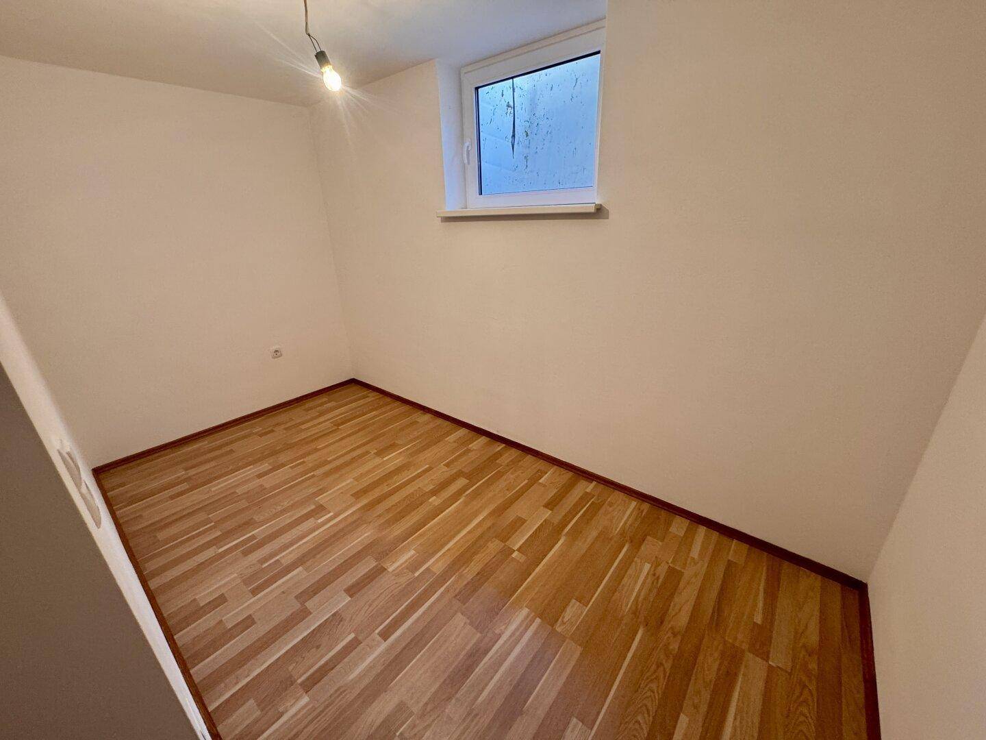 Kleines Schlafzimmer mit Laminatboden und Fenster, ideal als Kinder- oder Arbeitszimmer.