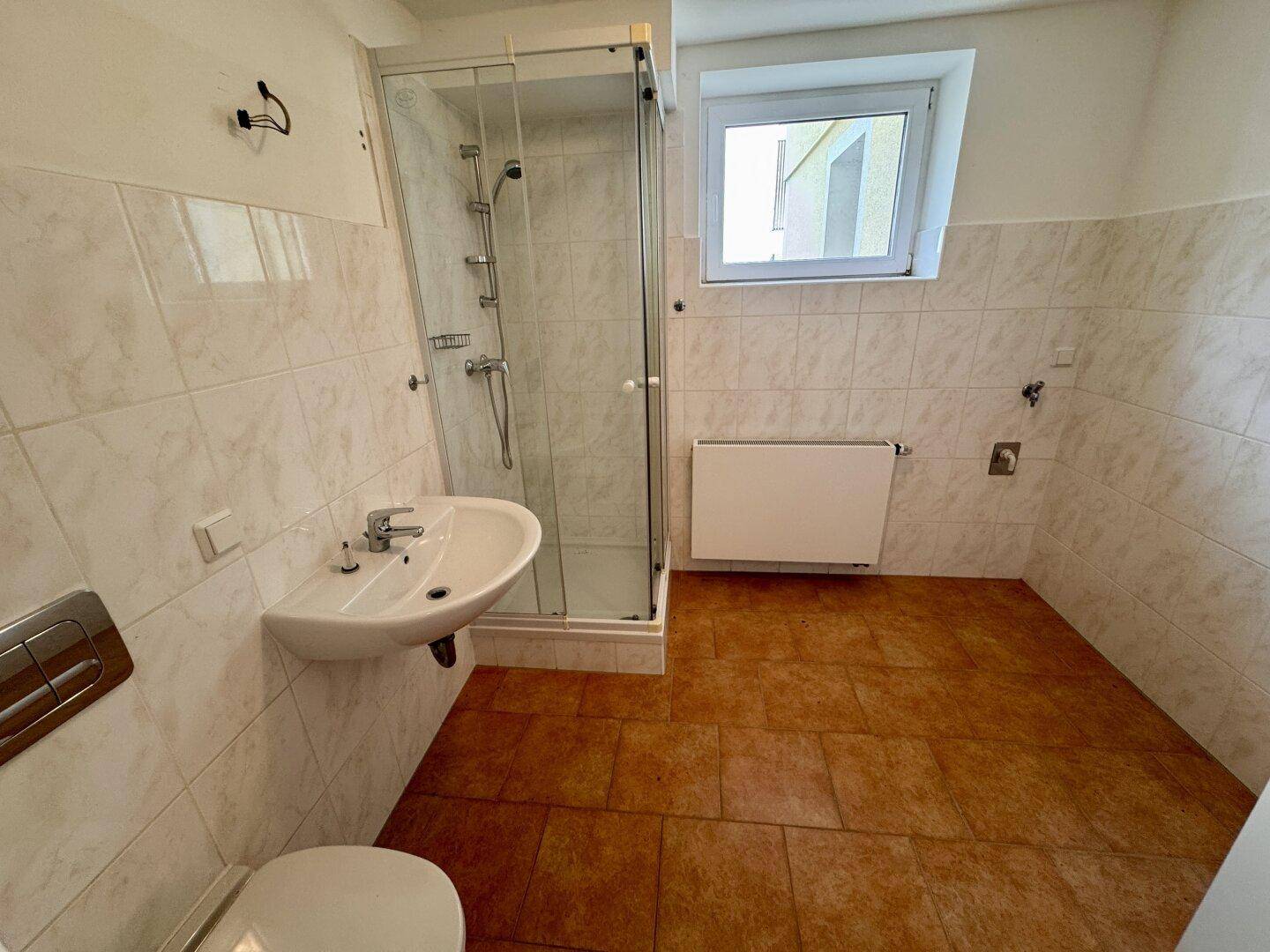 Badezimmer mit Duschkabine, Waschbecken und WC, gefliest in Beige und Braun.