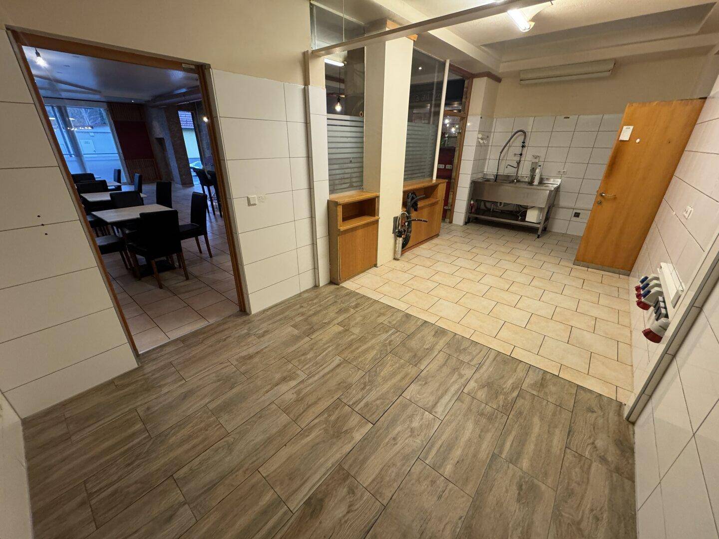 Ein Übergangsbereich mit unterschiedlichen Fliesenböden, der zu einer gefliesten Küche mit Spülbecken führt.
