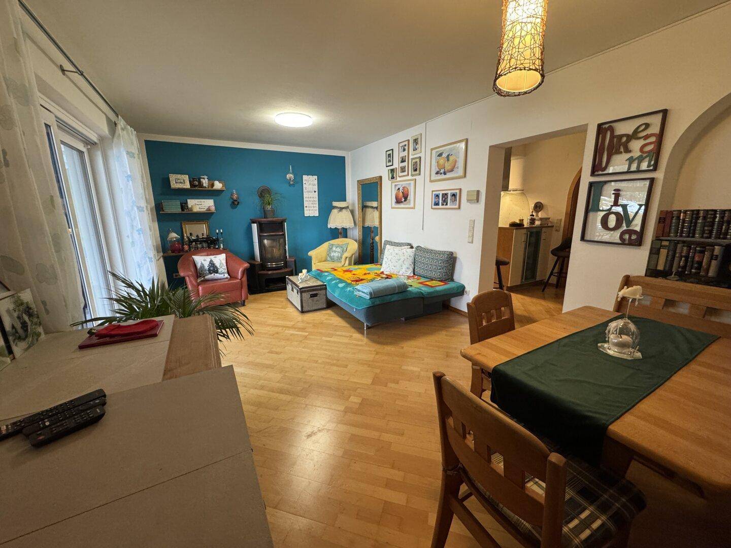 Wohn- und Essbereich mit Holzboden, farbiger Wand und Zugang zur Terrasse.