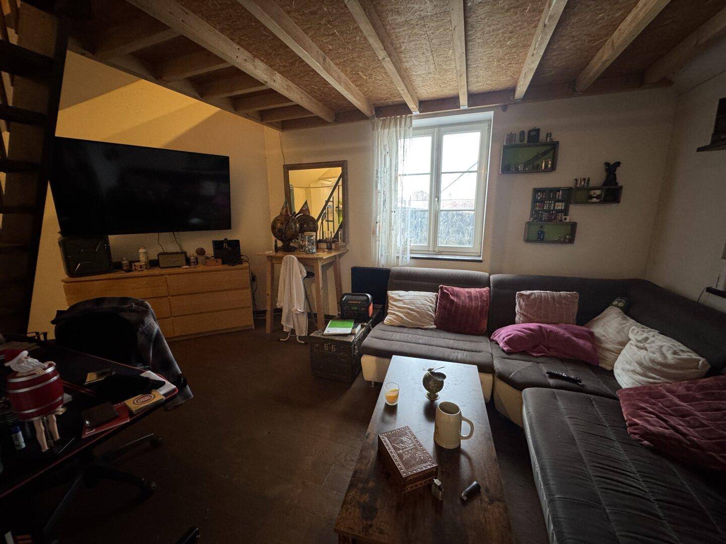 Rustikales Wohnzimmer mit sichtbaren Holzbalken, großem Fernseher und gemütlichem Sofa.