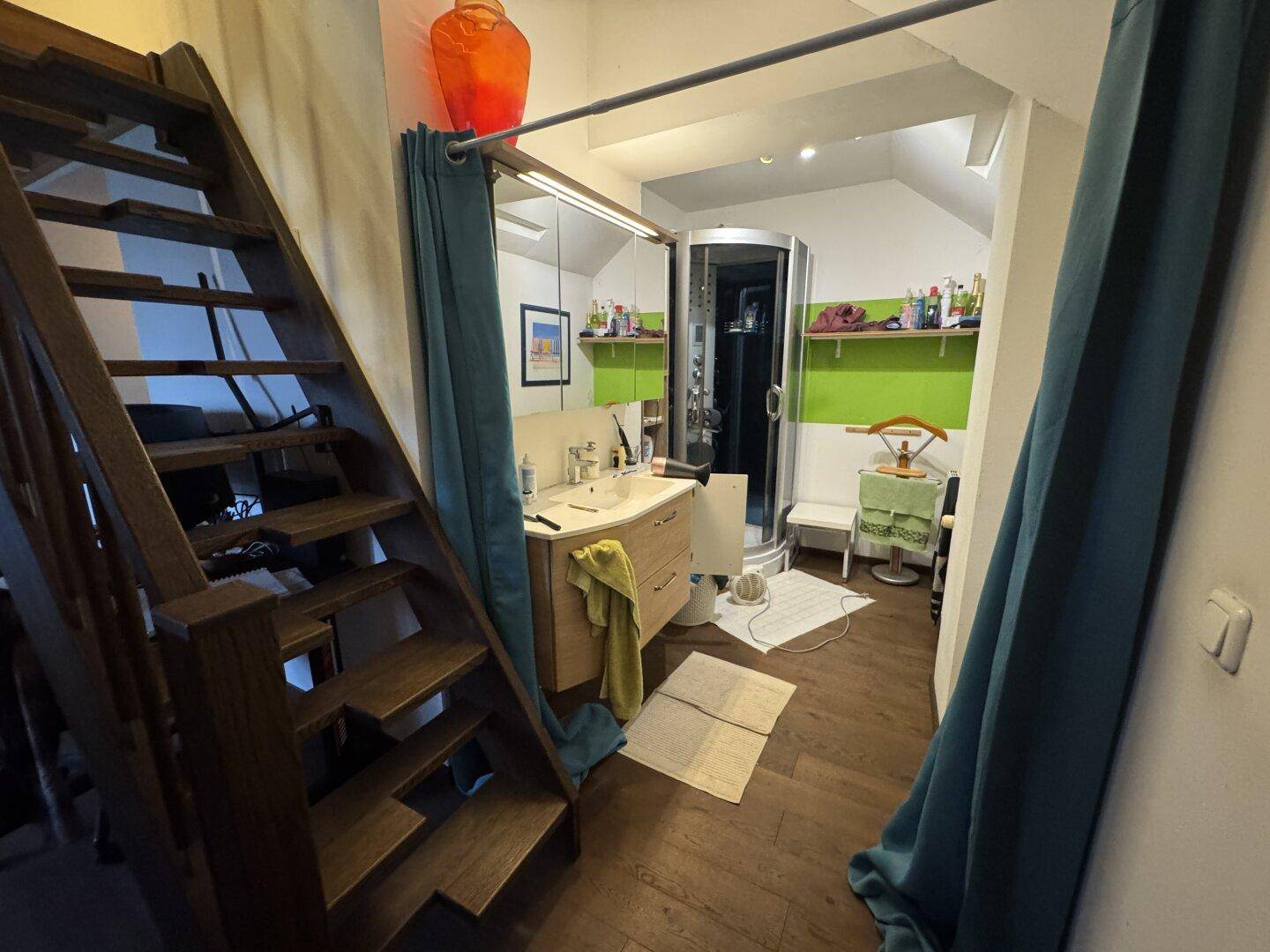 Badezimmer mit Duschkabine, Waschtisch und Holztreppe.