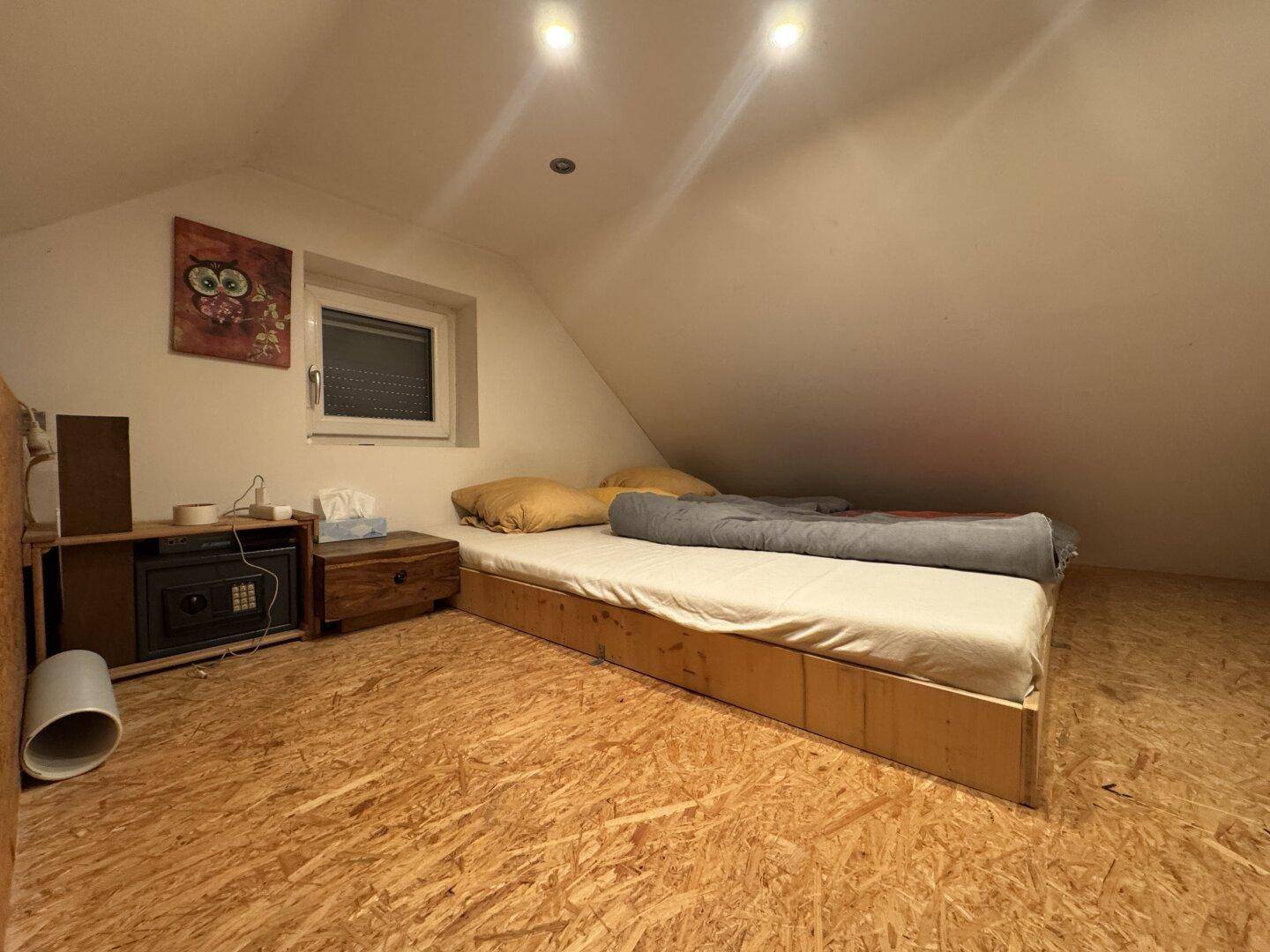 Einfaches Schlafzimmer mit Bett, OSB-Boden und Dachschräge.