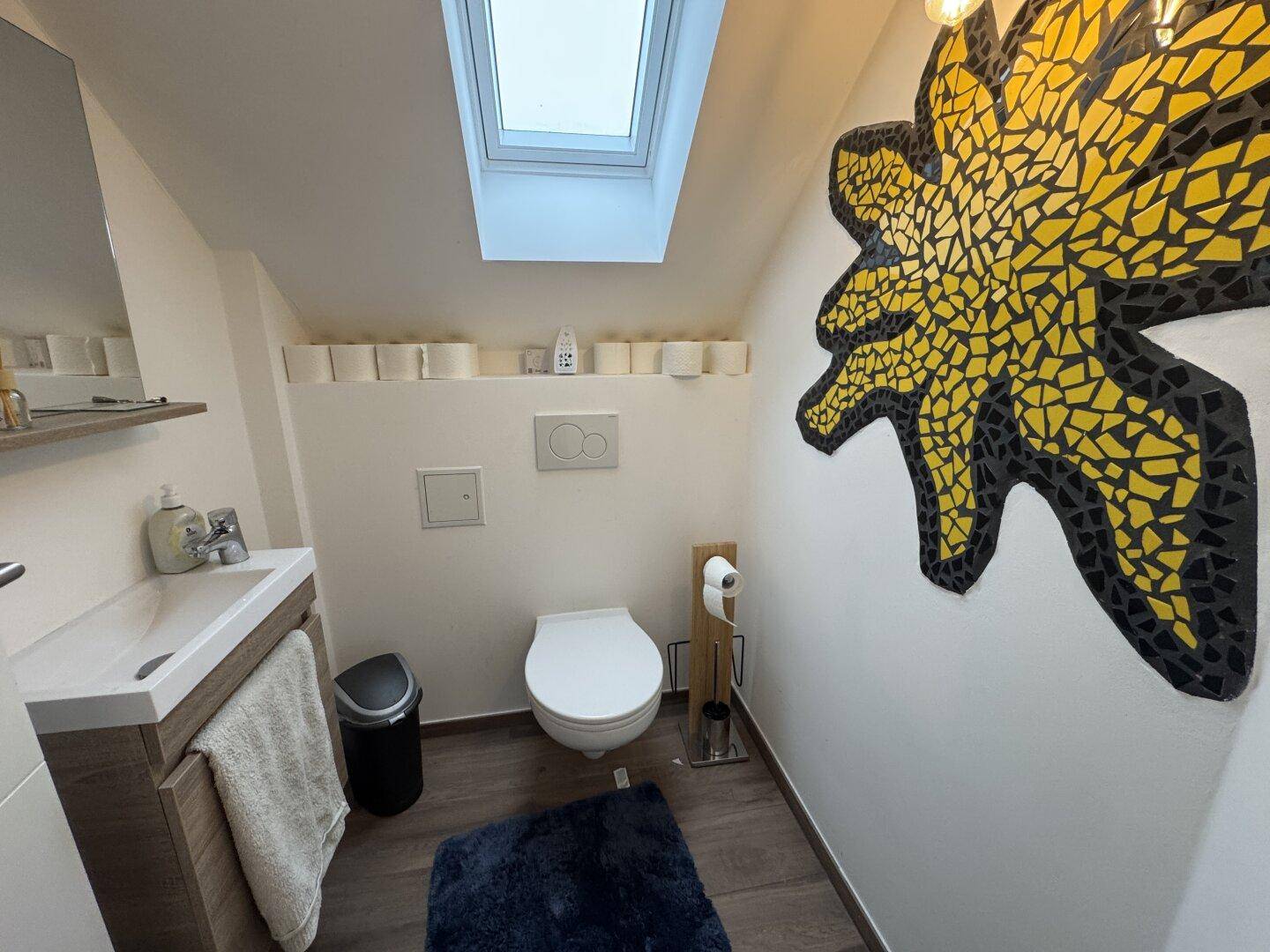 Kleines Gäste-WC mit modernem Waschtisch, Toilette und farbiger Wanddekoration.