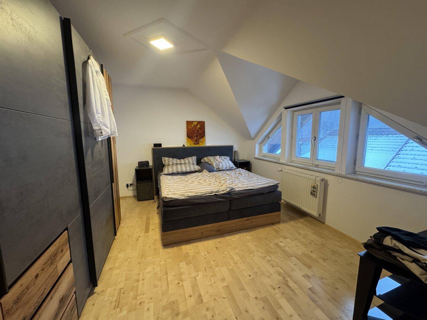 Gemütliches Schlafzimmer mit Holzboden, Kleiderschrank und Dachschrägenfenstern.