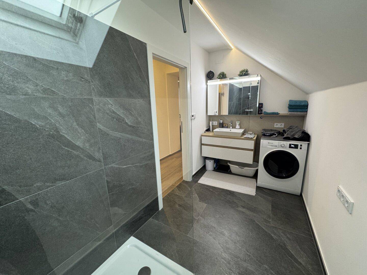 Modernes Badezimmer mit Waschtisch, Spiegel und Waschmaschine unter Dachschräge.