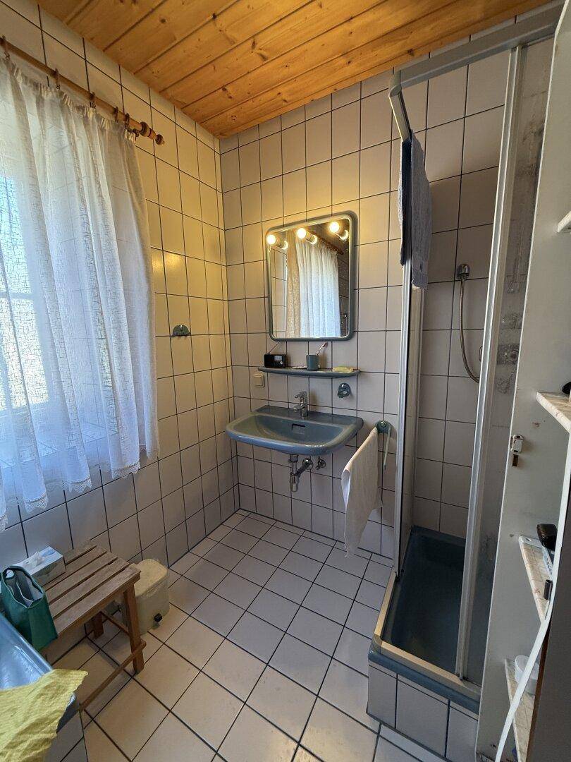 Badezimmer mit Duschkabine, Waschbecken und Holzdecke, ausgestattet mit einem Fenster für Tageslicht.