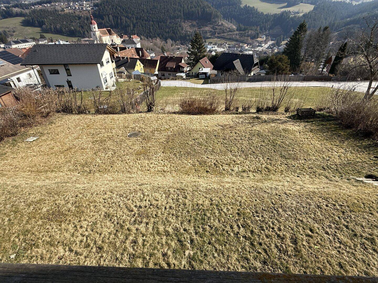 Großer Gartenbereich mit Rasenfläche und Blick auf das Dorf und die umliegenden Berge.