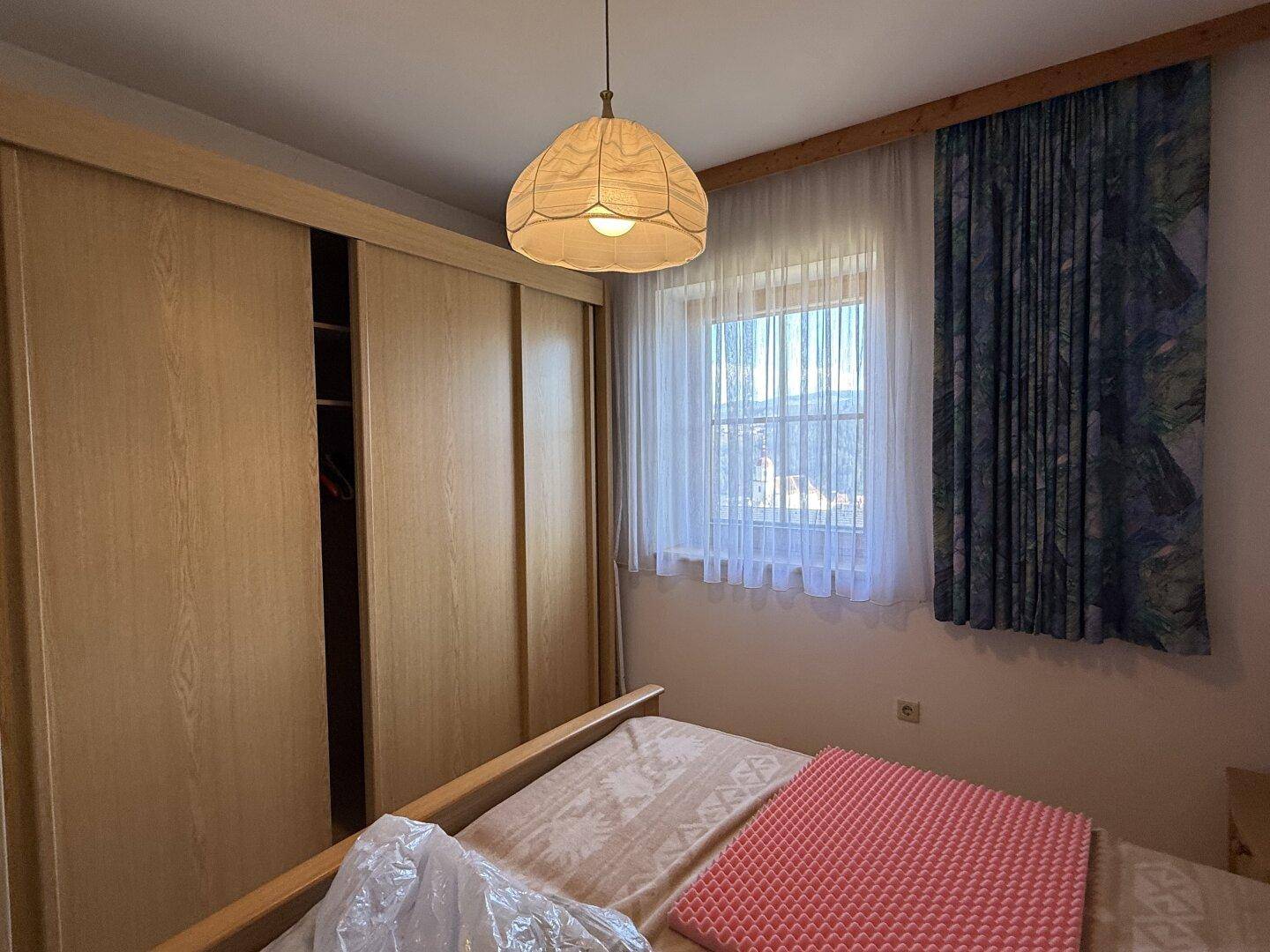 Schlafzimmer mit Holzboden, Einbauschrank und Fenster mit Vorhängen, bietet eine gemütliche Atmosphäre.