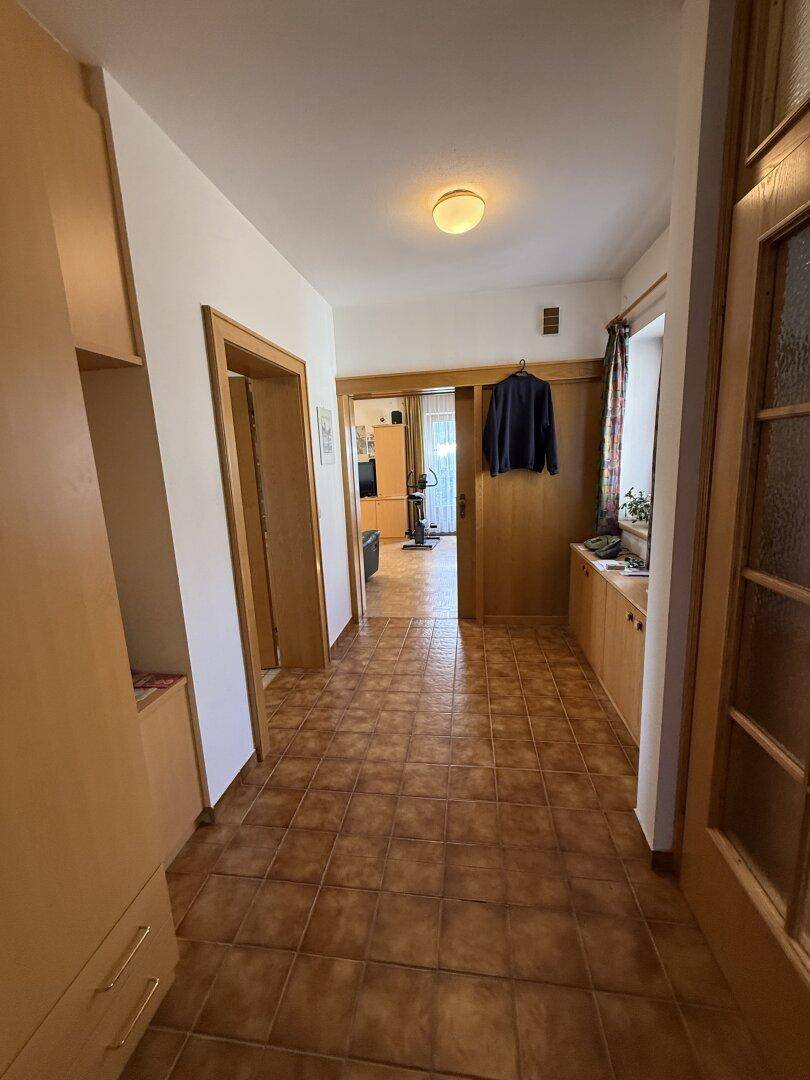 Langer Flur mit Fliesenboden, Holzmöbeln und Blick in den Wohnbereich, der viel Platz bietet.