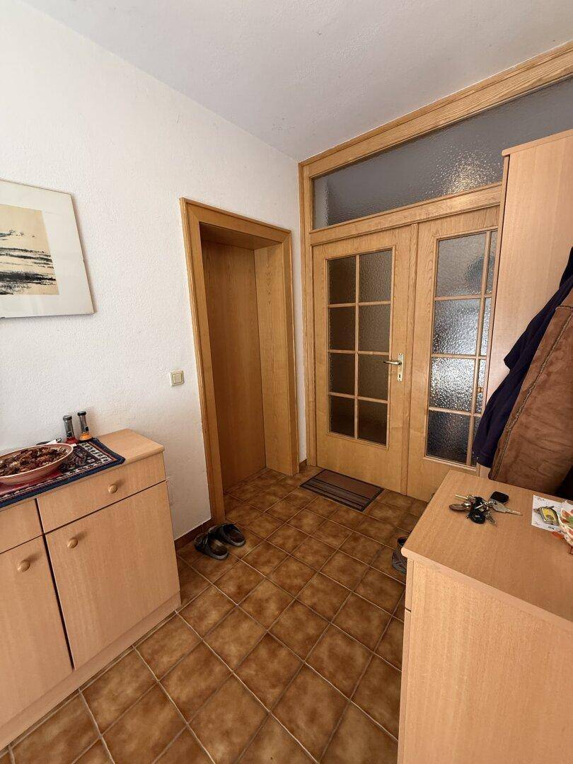 Eingangsbereich mit Fliesenboden, Holzmöbeln und einer Holztür mit Glaseinsätzen.