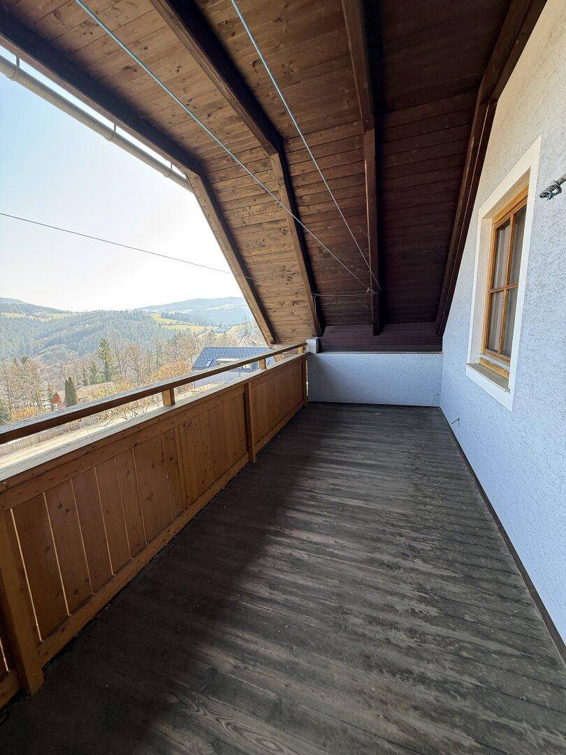 Überdachter Balkon mit Holzboden und weitem Blick auf die umliegende Landschaft und die Berge.