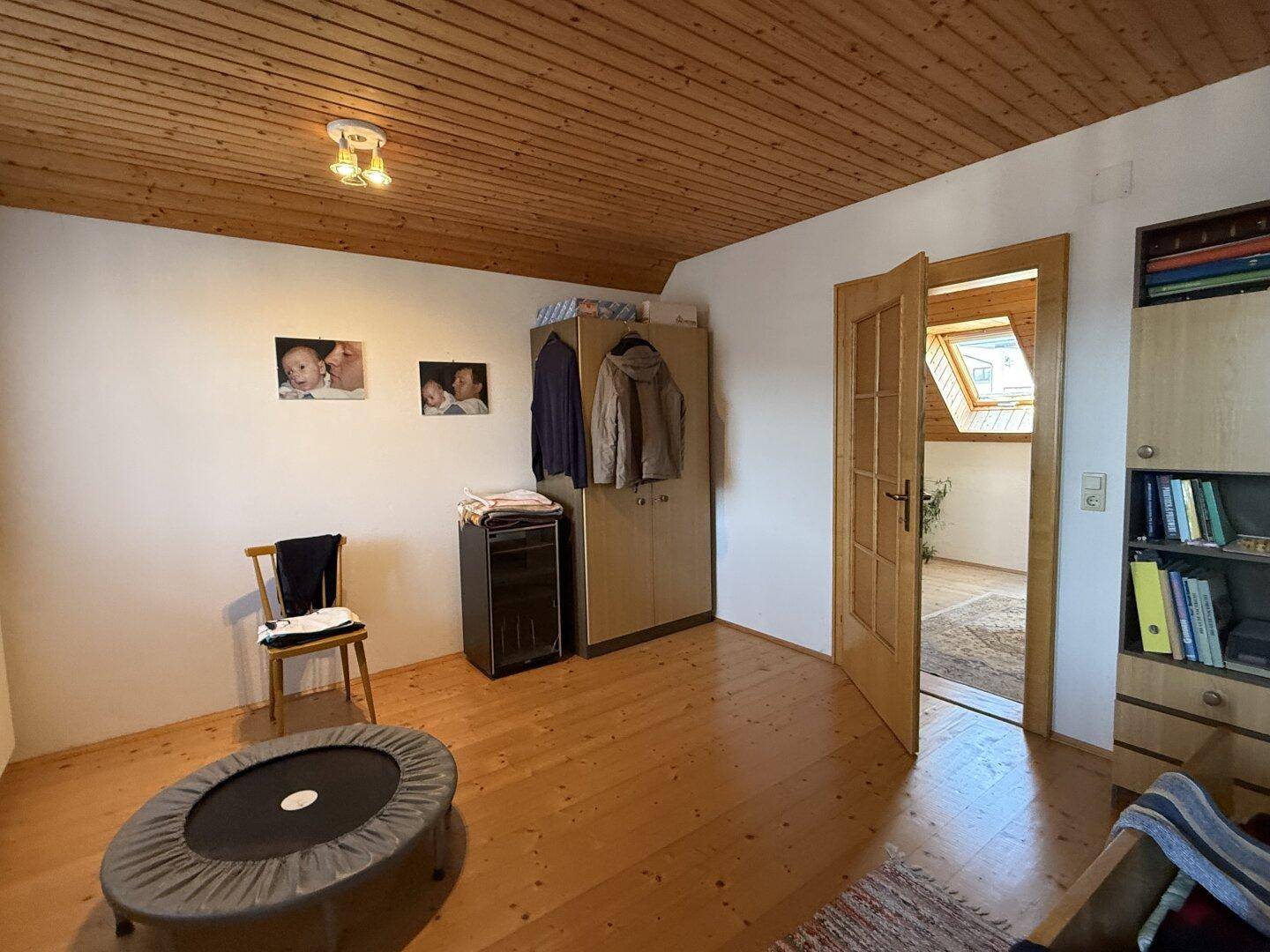 Kinderzimmer im Dachgeschoss mit Holzboden, Holzdecke und Zugang zu einem weiteren Raum.