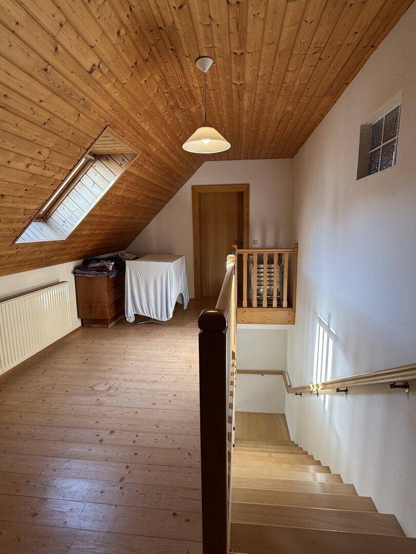 Heller Dachbodenbereich mit Holzdecke, Holzboden und Treppenabgang, der zusätzlichen Wohnraum bietet.