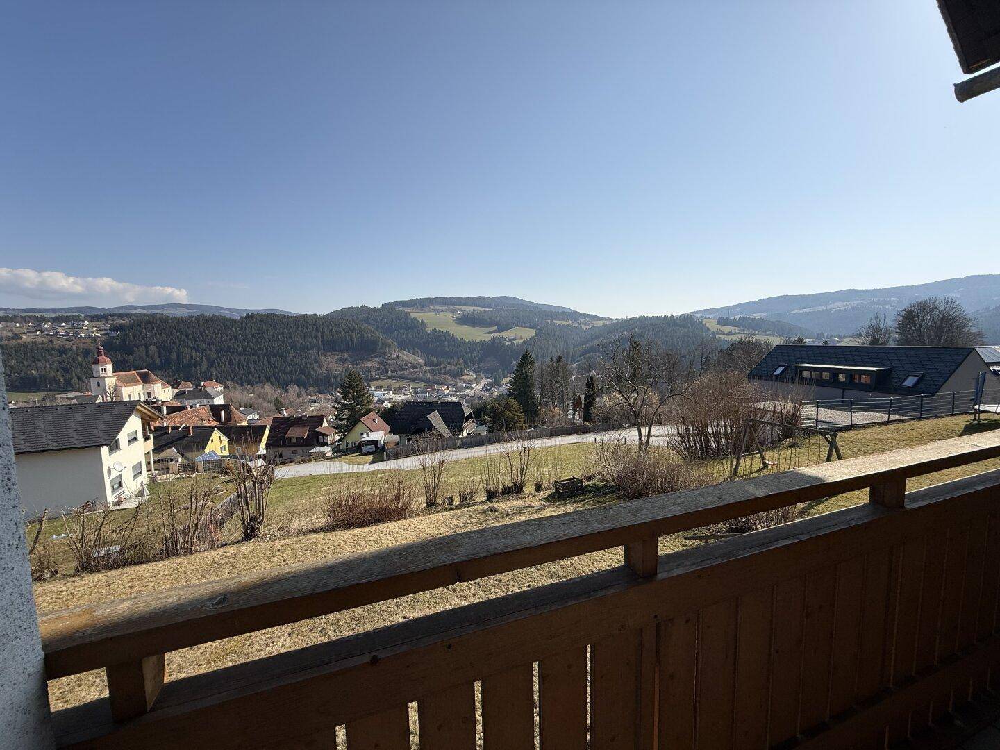 Balkon mit Holzboden und weitem Blick über die umliegende Landschaft und das malerische Dorf.