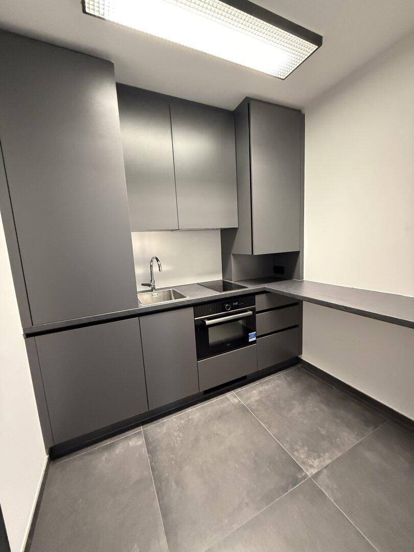 Moderne, kompakte Küchenzeile in Grau mit integriertem Backofen und Spüle, ideal für kleine Büros.
