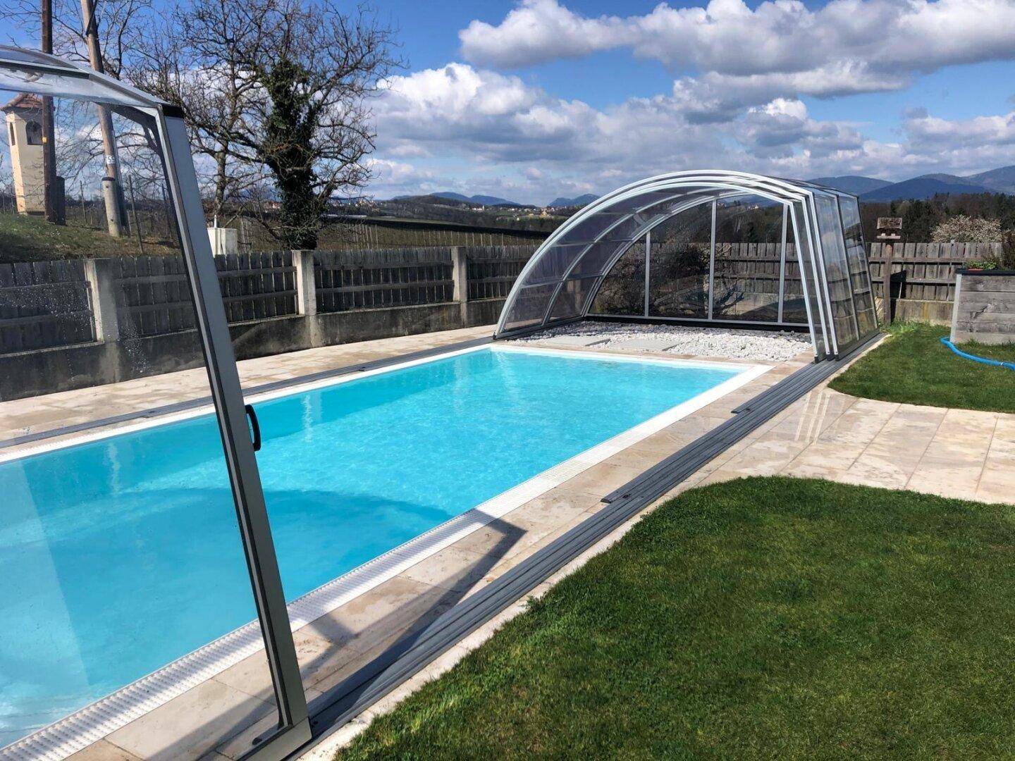 Großer Außenpool mit Überdachung und gepflegter Rasenfläche unter blauem Himmel.