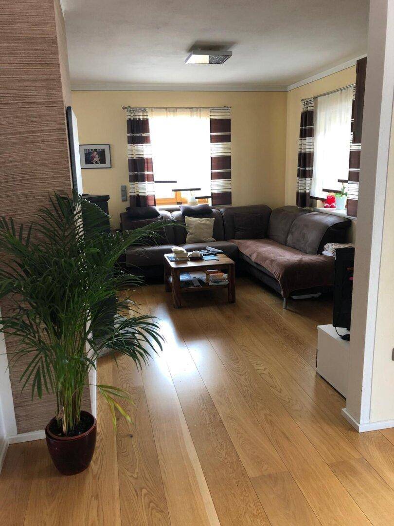Gemütliches Wohnzimmer mit Holzboden, bequemer Sofagarnitur und mehreren Fenstern.