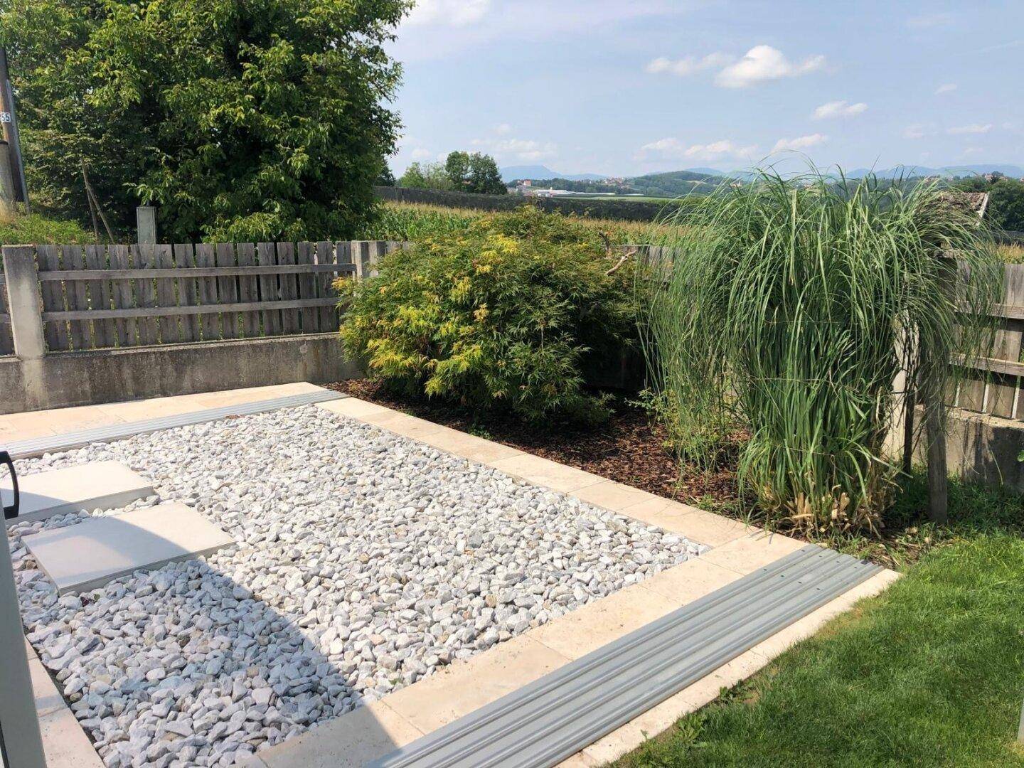 Gartenbereich mit Kiesfläche, Ziergräsern und Blick auf die umliegende Landschaft.