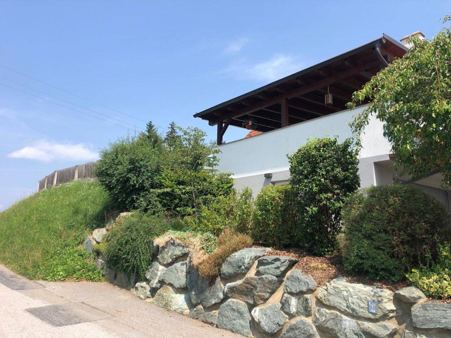 Außenansicht des Hauses mit Steingarten und üppiger Bepflanzung am Hang.