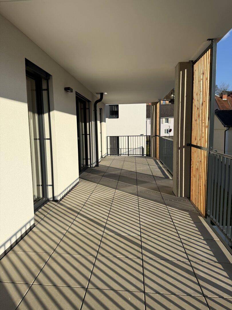 Langer Balkon mit Fliesenboden, modernen Holzlamellen und viel Sonnenschein.
