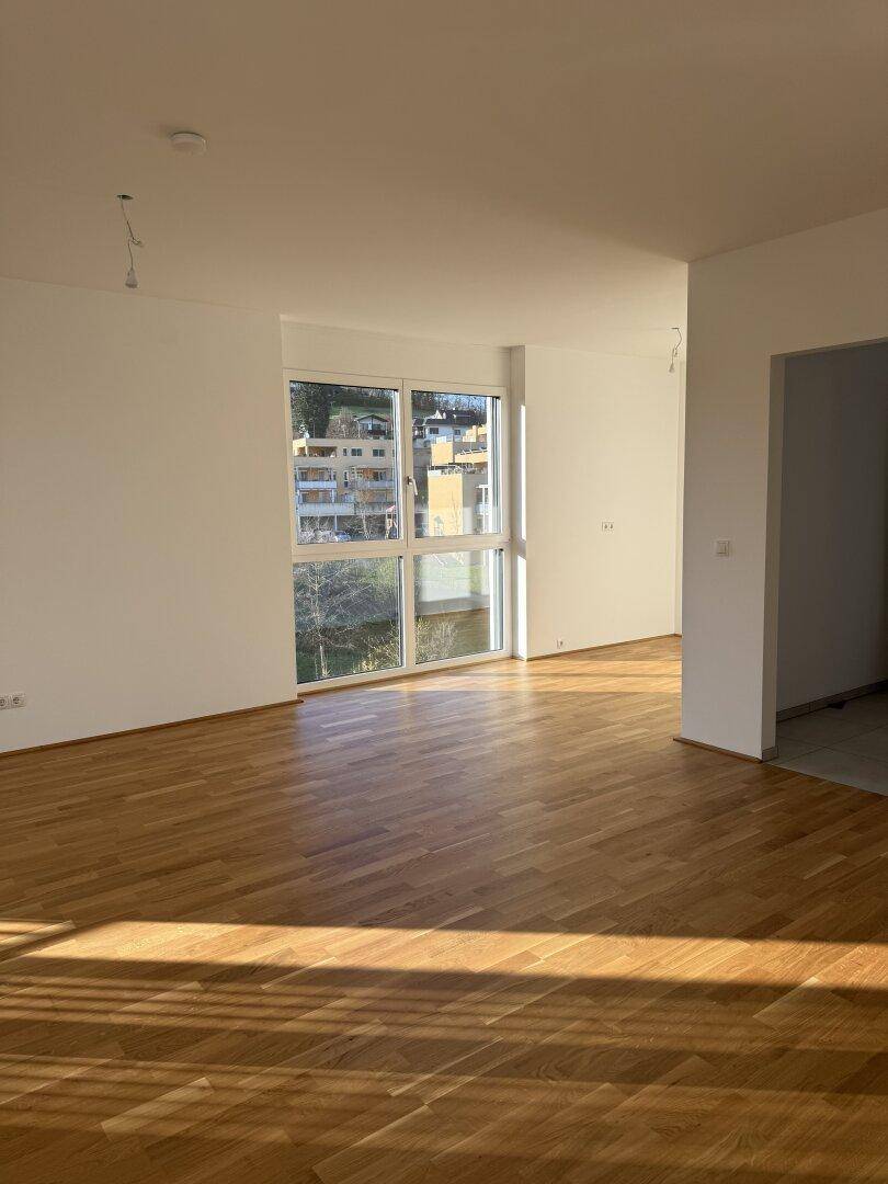 Heller Wohnraum mit Eichenparkettboden und großen Fenstern mit Blick ins Grüne.