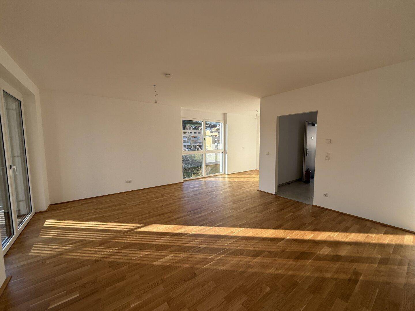 Lichtdurchfluteter Wohnbereich mit hellem Parkettboden und Zugang zu weiteren Räumen.