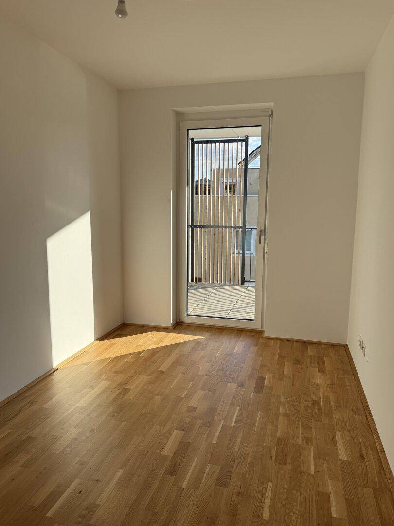 Sonnenverwöhntes Zimmer mit Parkettboden und Zugang zu einem Außenbereich.