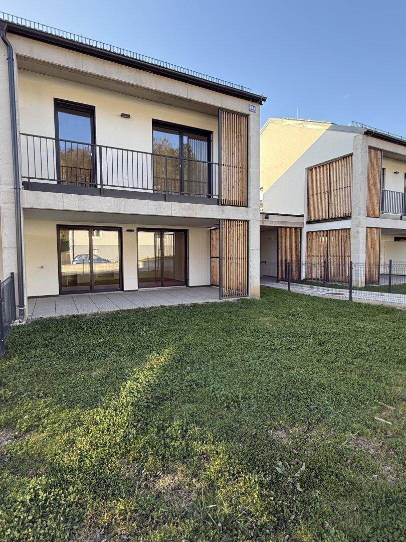 Ansicht der modernen Gebäudefassade mit Balkon, Terrasse und Rasenfläche im Vordergrund.