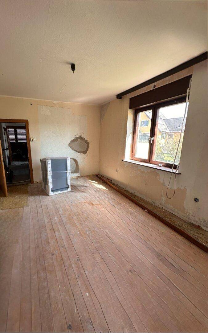 Zimmer im Renovierungszustand mit Holzdielenboden und Fenster, bereit für neue Gestaltung.