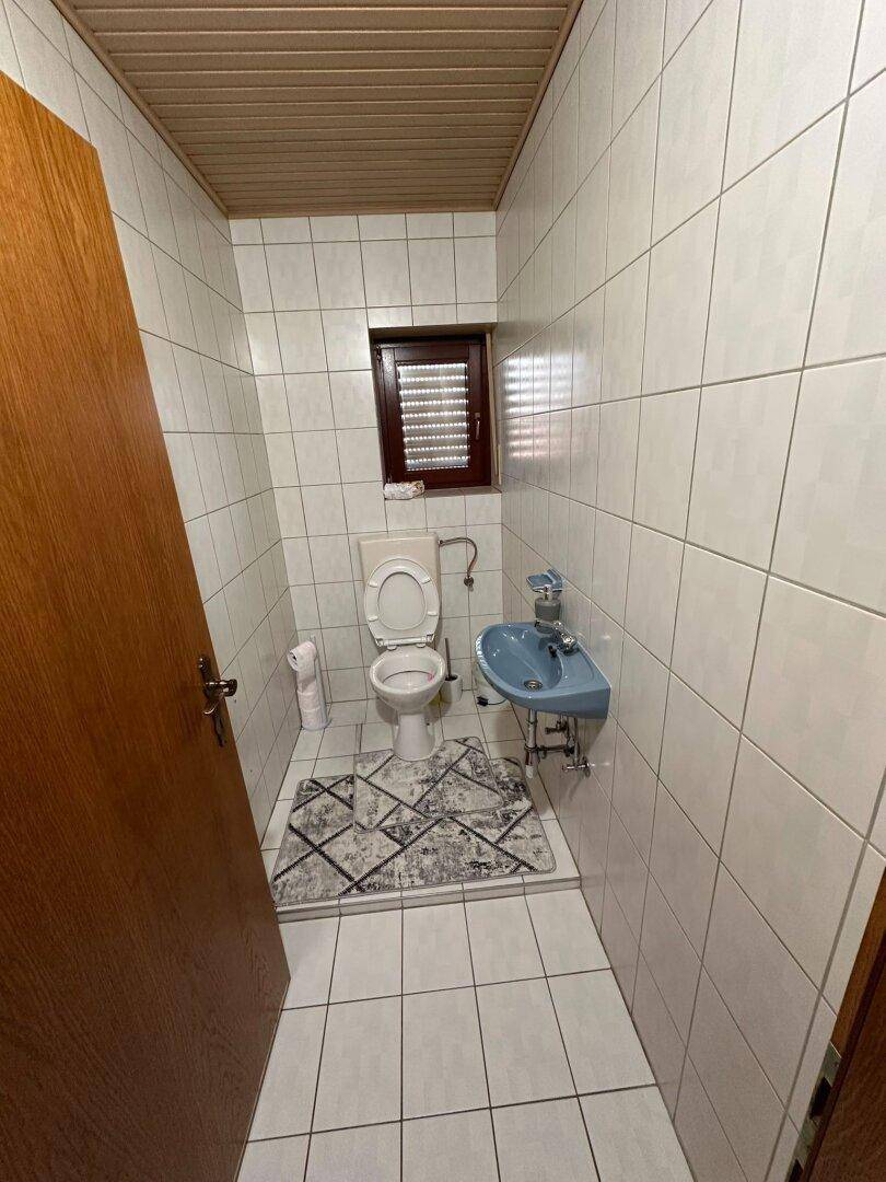 Kleines Gäste-WC mit hellblauen Fliesen, WC und Waschbecken, sowie einem Fenster.