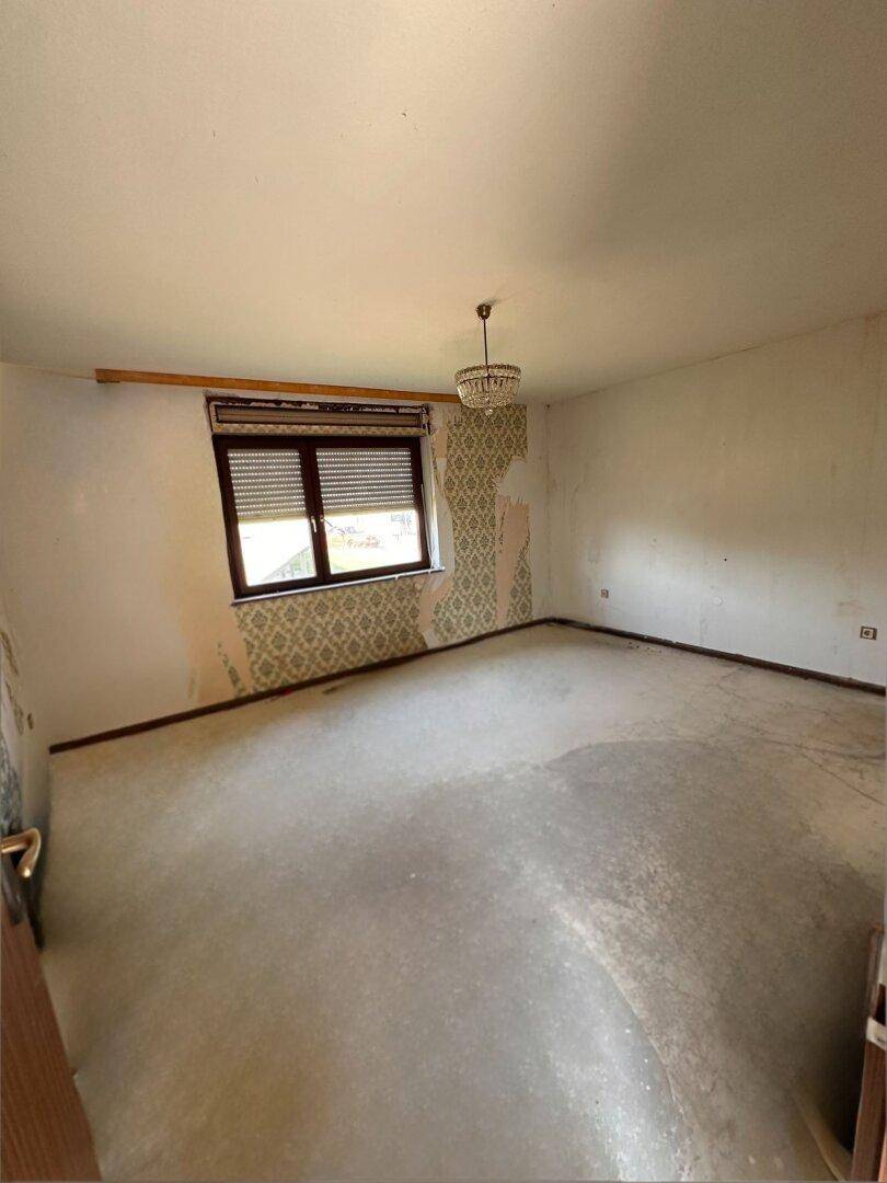 Leeres Zimmer im Renovierungszustand mit Fenster und Resten alter Tapete.