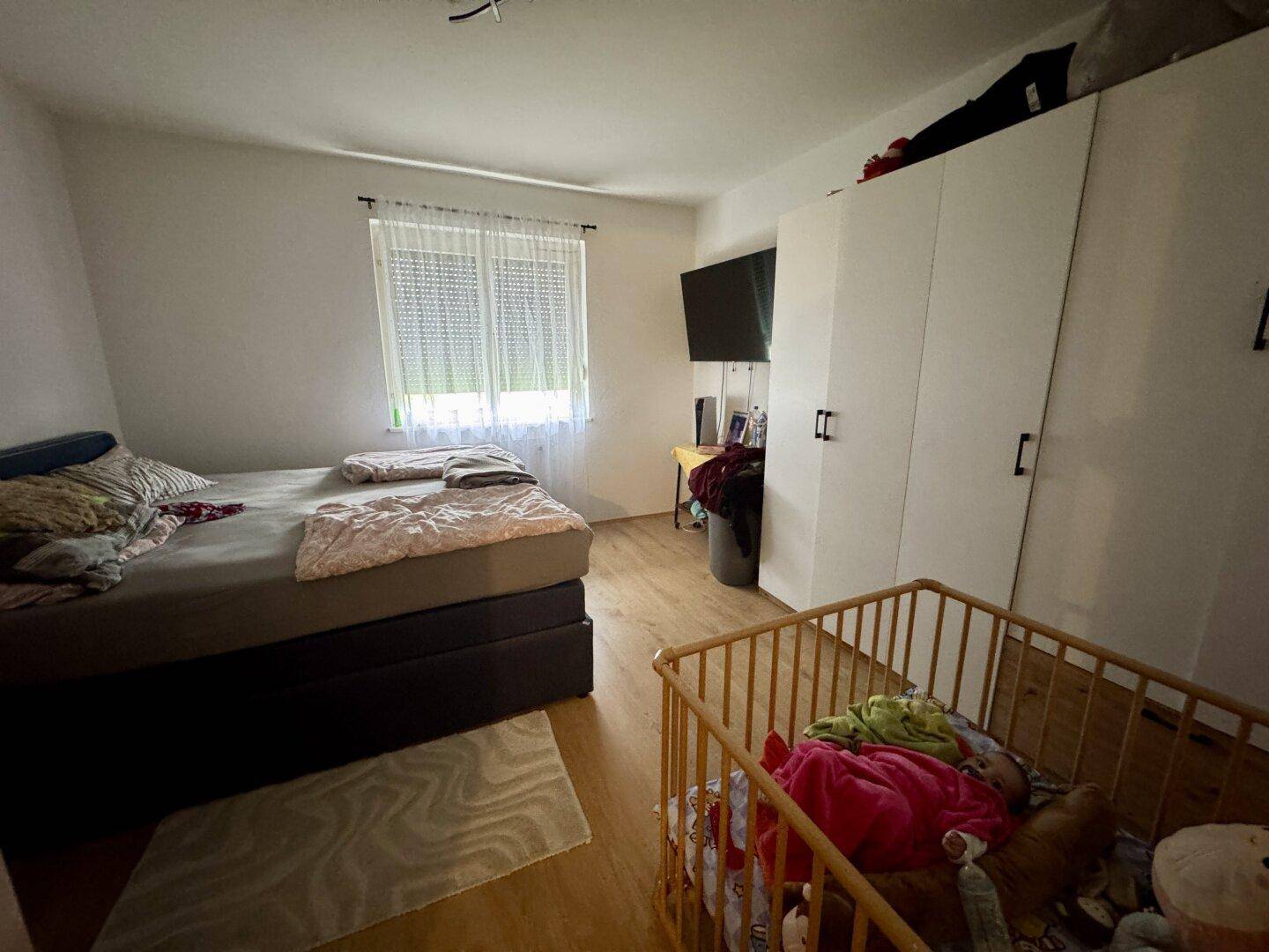 Helles Schlafzimmer mit Doppelbett, Kleiderschrank und Kinderbett, ausgestattet mit Laminatboden.