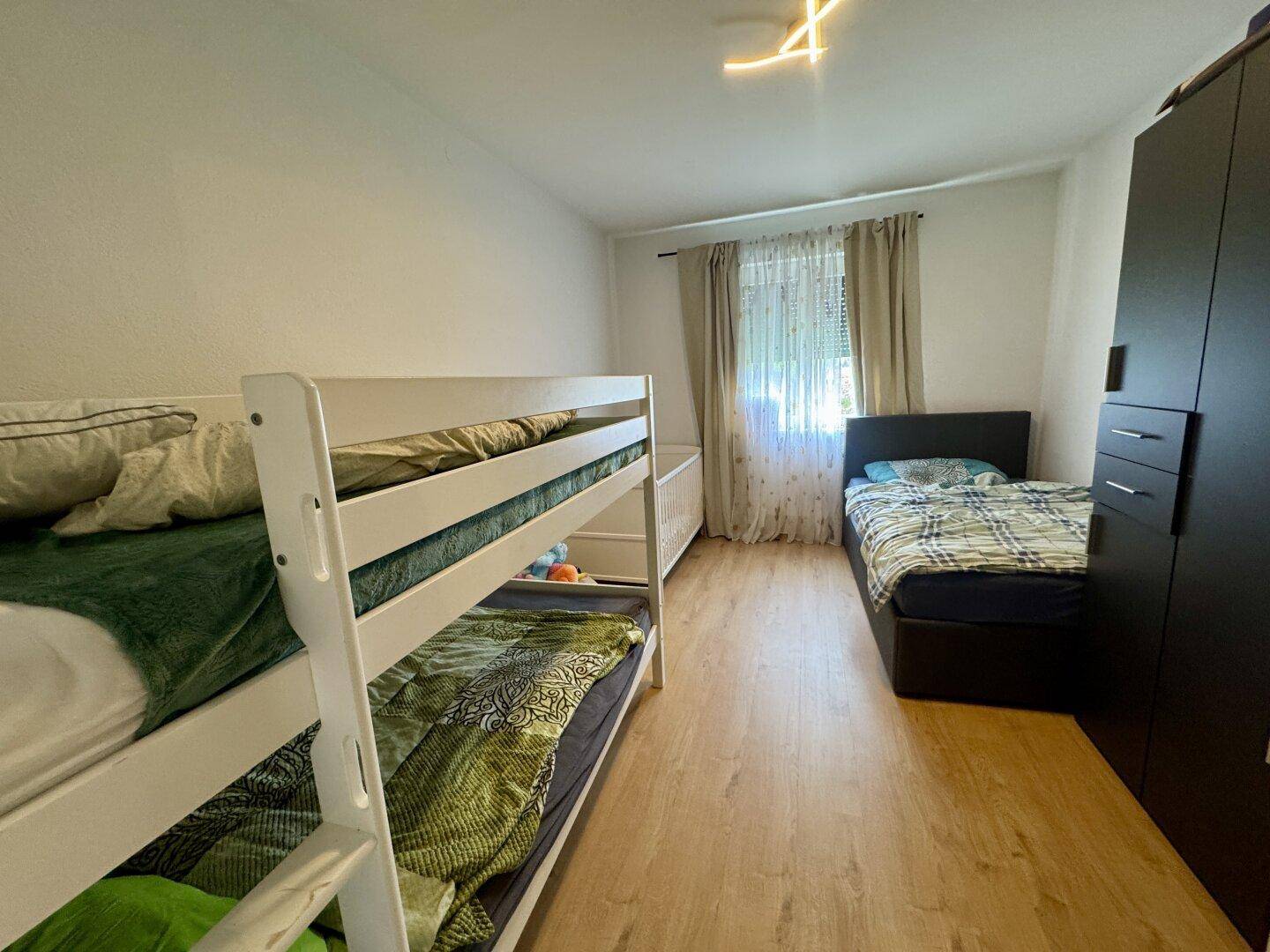 Helles Kinderzimmer mit Etagenbett, Einzelbett und dunklem Kleiderschrank, ideal für Geschwister.