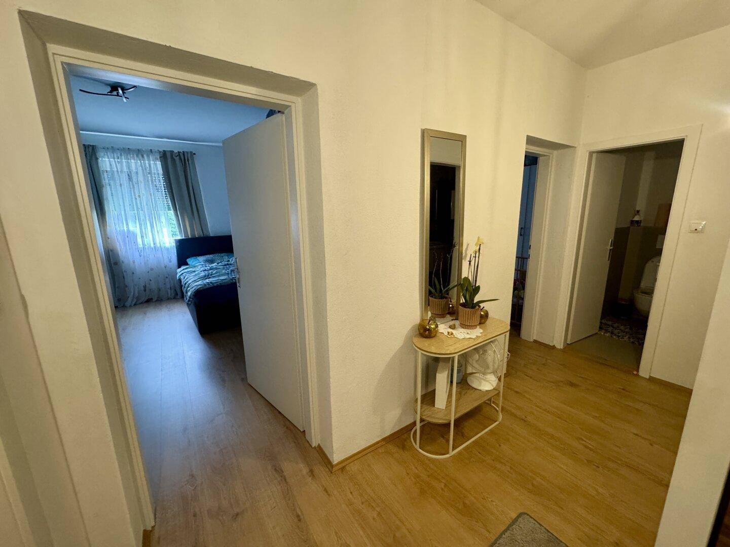 Heller Flur mit Laminatboden, einem kleinen Beistelltisch und Zugang zu weiteren Zimmern.
