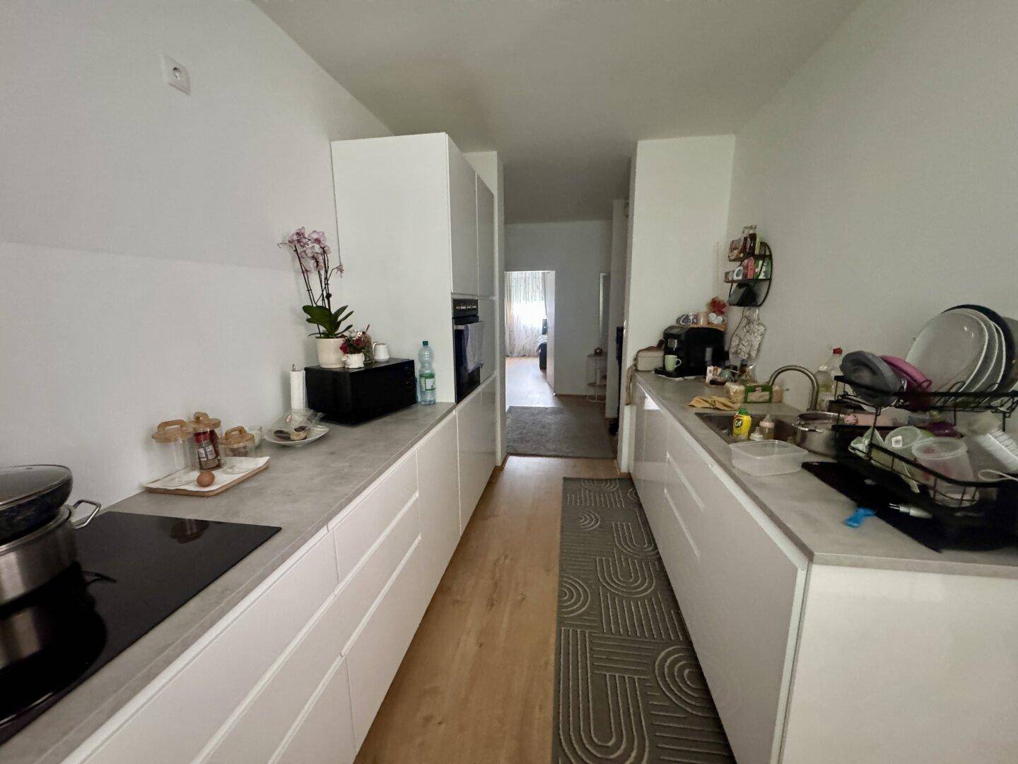 Moderne Küche mit weißen Schränken, integrierten Geräten und hellem Laminatboden.