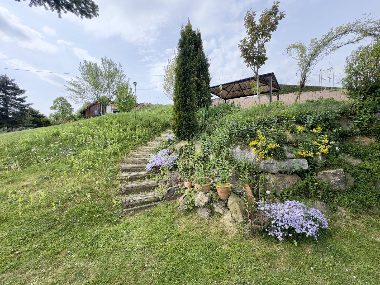 Naturbelassener Gartenhang mit Steinstufen, Blumenbeeten und üppiger Vegetation.