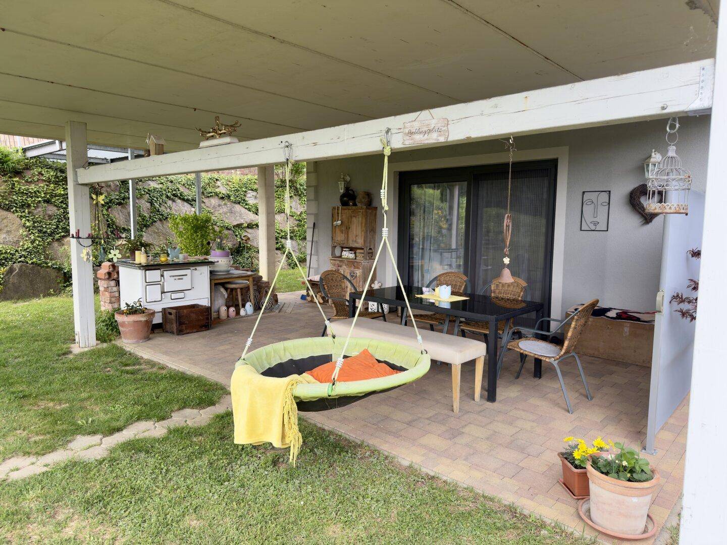 Überdachte Terrasse mit Essbereich, Schaukel und traditionellem Ofen im Freien.
