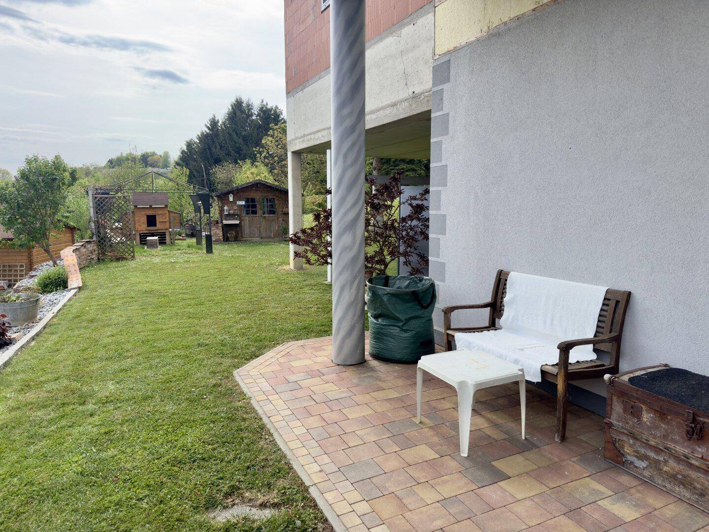 Gepflasterter Außenbereich mit Sitzbank und kleinem Tisch neben dem Haus.