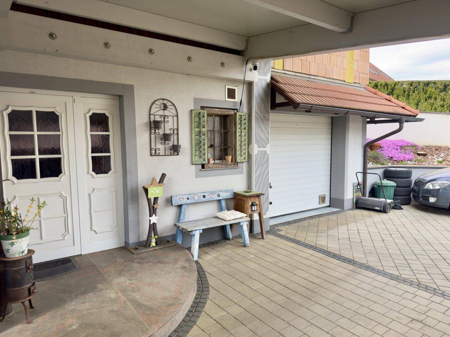 Eingangsbereich des Hauses mit weißer Doppeltür, Fenster und Zugang zur Garage.