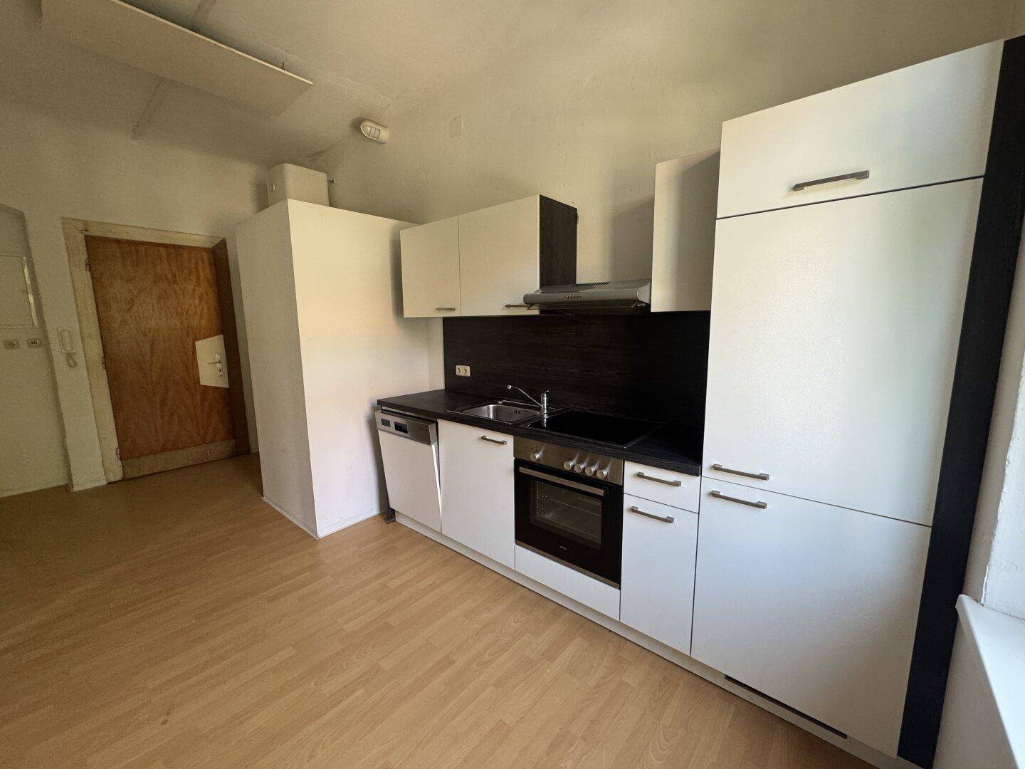 Funktionale Küchenzeile mit weißen Fronten, dunkler Arbeitsplatte und Laminatboden in einem hellen Raum.