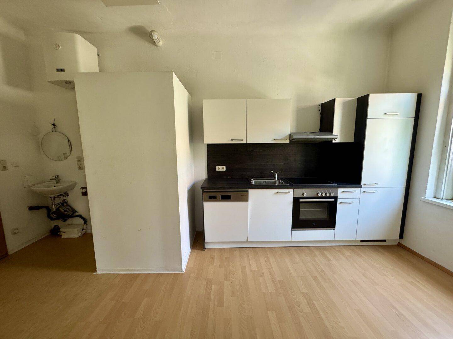 Kompakte Küchenzeile mit weißen Schränken und integrierten Geräten in einem hellen Raum mit separatem Waschbecken.