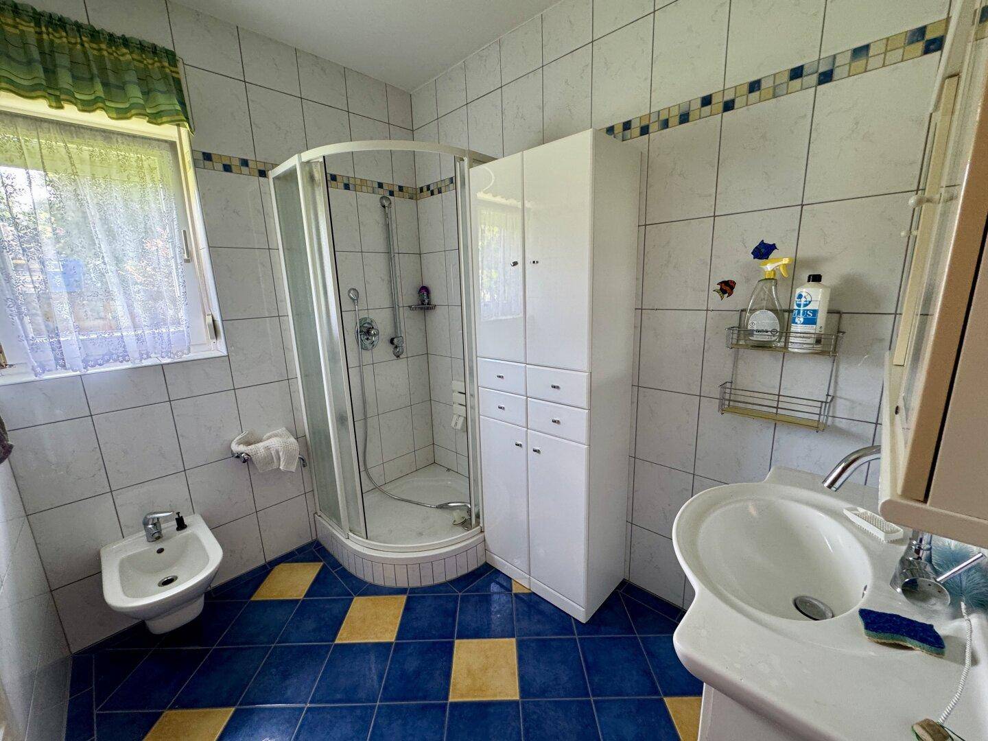 Badezimmer mit Dusche, Bidet, Waschbecken und farbigen Fliesen im Stil der 80er Jahre.