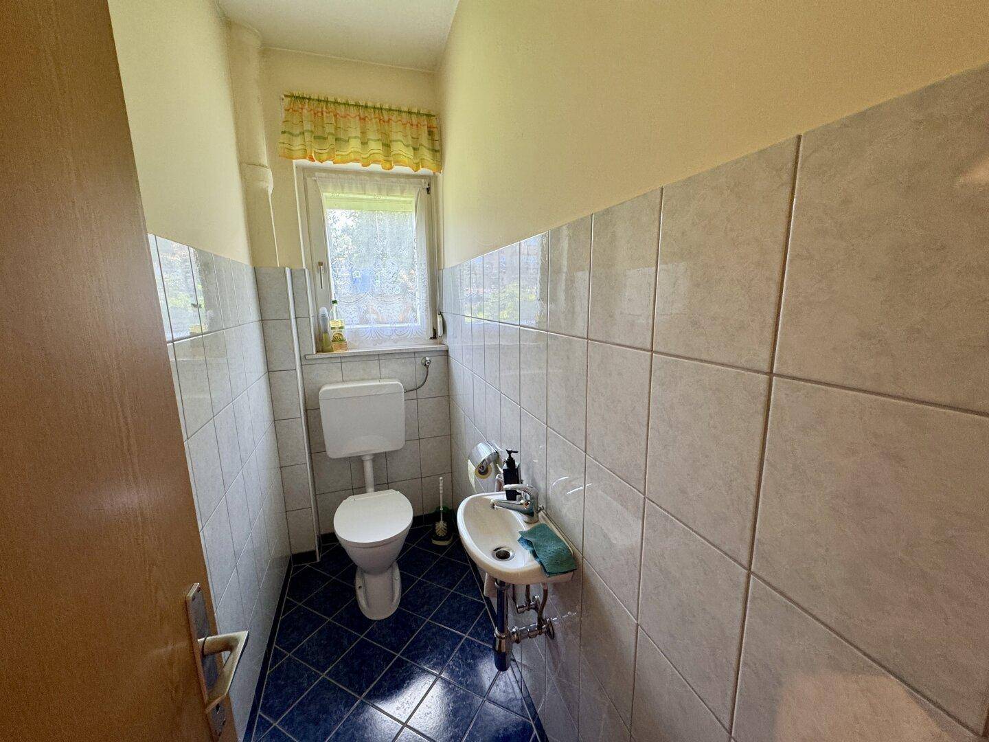 Kleines Gäste-WC mit blauen Bodenfliesen und Fenster.