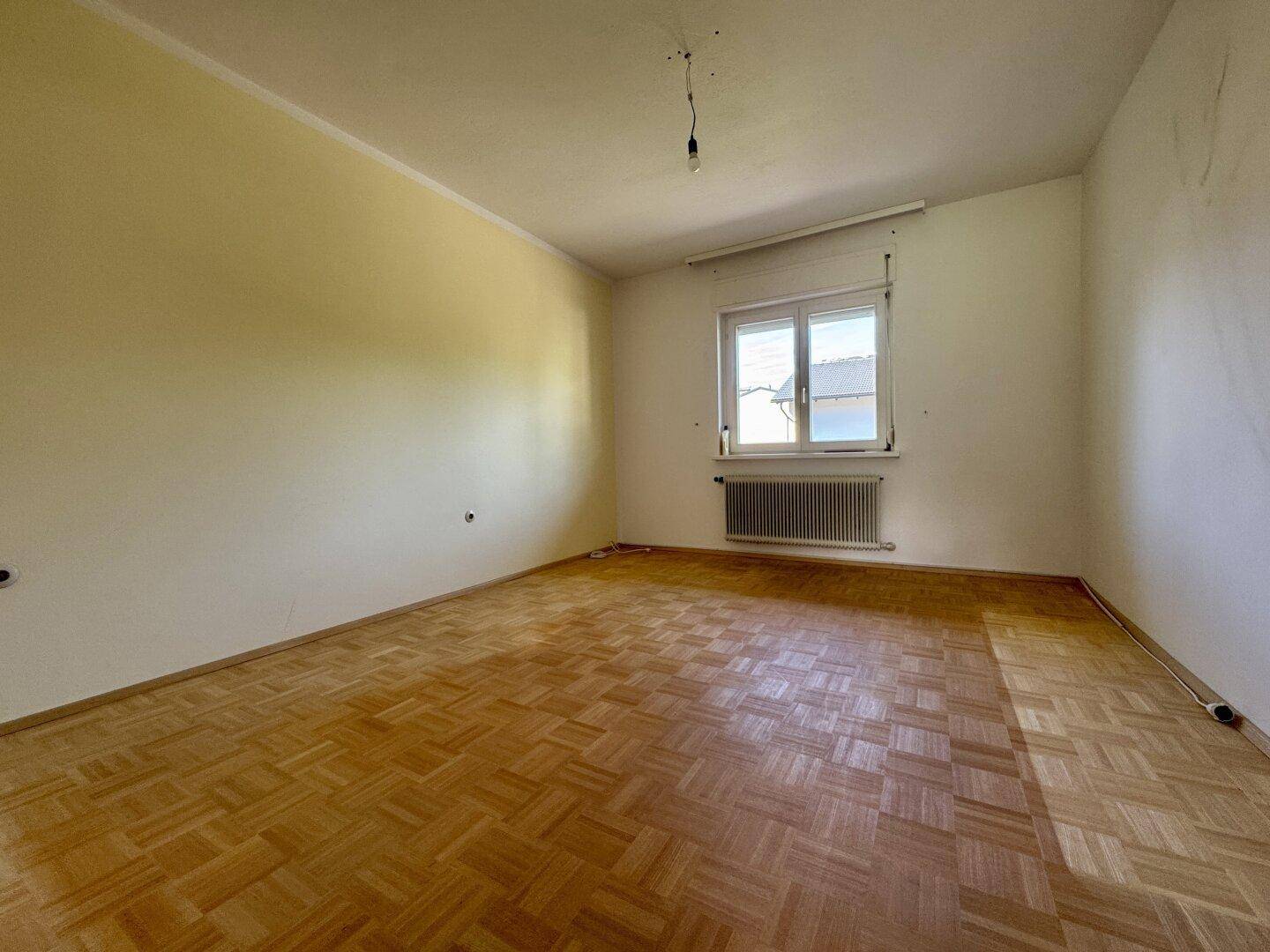 Leeres Zimmer mit Parkettboden, gelben Wänden und Fenster, bereit zur individuellen Gestaltung.