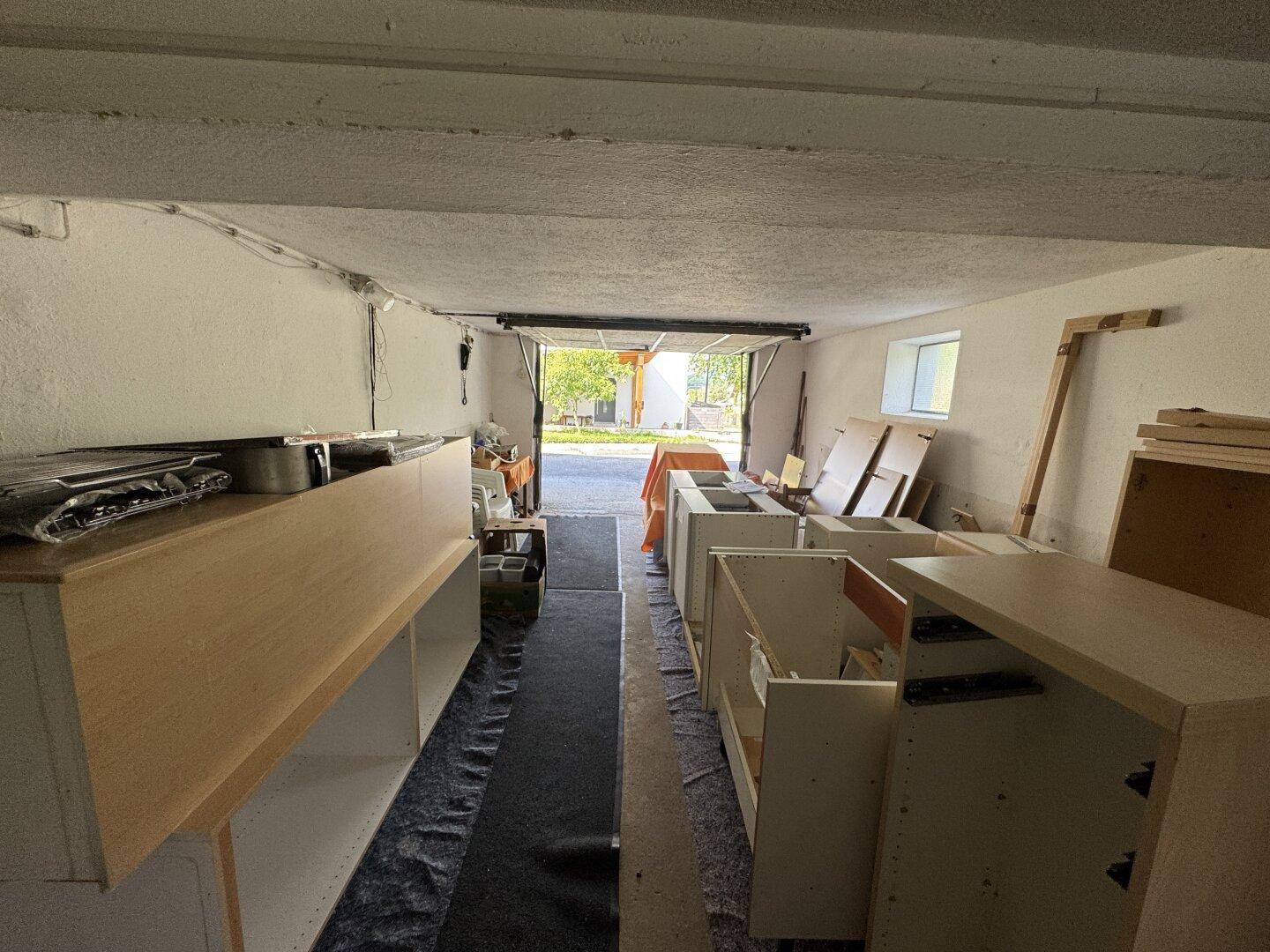 Garage mit geöffnetem Tor, als Lagerraum genutzt und Blick nach draußen.