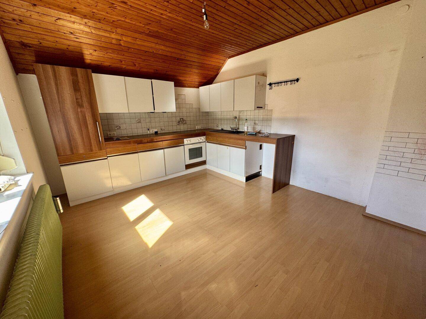 Dachgeschossküche mit Holzbalkendecke, Laminatboden und Einbauküche unter der Dachschräge.