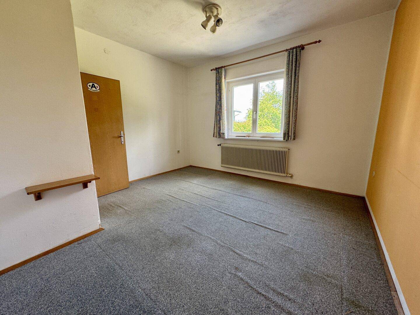 Schlafzimmer mit Teppichboden, Fenster und schlichten Vorhängen, bietet einen grünen Ausblick.
