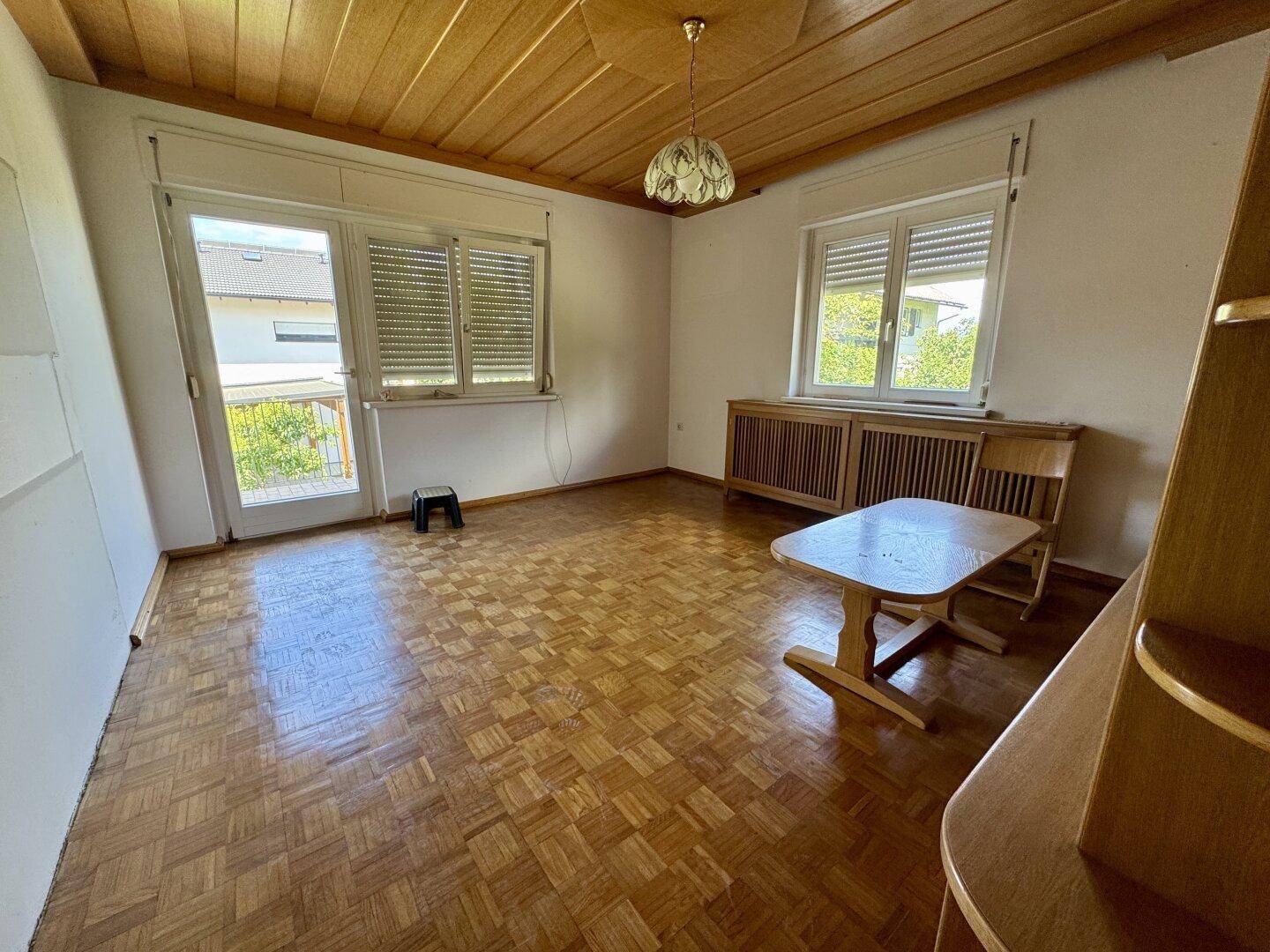 Helles Wohnzimmer mit Parkettboden, Holzdecke und Zugang zum Außenbereich.